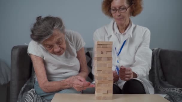 Volwassen arts die sessie, therapie voor senior patiënt in verpleeghuis, training fijne motoriek voor dementie, alzheimer ziekte en herstel instituut door het vouwen van houten blokken, spelen — Stockvideo