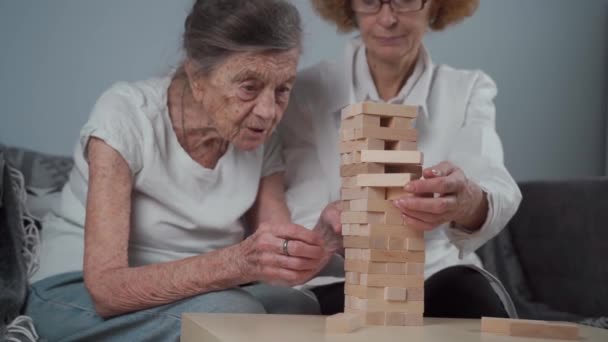 Terapia demencji w zabawny sposób, trening palców i umiejętności motoryczne, budowanie drewnianych klocków do wieży, gra Jenga. Starsza kobieta 90 lat i lekarz gra edukacyjna w domu opieki — Wideo stockowe