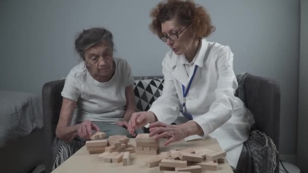 Volwassen arts die sessie, therapie voor senior patiënt in verpleeghuis, training fijne motoriek voor dementie, alzheimer ziekte en herstel instituut door het vouwen van houten blokken, spelen — Stockvideo