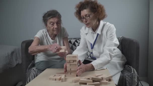 Sessione di conduzione di medici maturi, terapia per pazienti anziani in casa di cura, formazione di abilità motorie fini per la demenza, malattia di Alzheimer e istituto di recupero piegando blocchi di legno, giocando a jenga — Video Stock