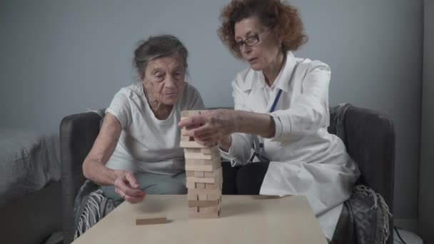 成熟した医師によるセッション、老人ホームでの高齢者のための治療、認知症、アルツハイマー病および回復研究所のための優れた運動能力を訓練する木製のブロックを折り畳むことによって、演奏 — ストック動画