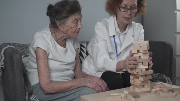 Demencia terápia játékos módon, edzés ujjak és finom motoros készségek, épít fa blokkok torony, játék. Idősebb nő 90 éves és az orvos oktatási játékot idősek otthonában — Stock videók
