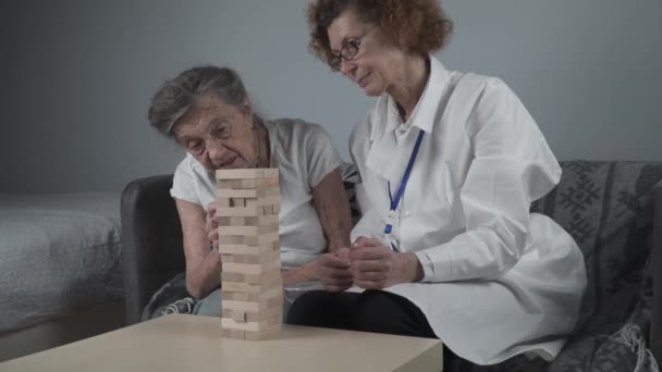 Demence terapie hravým způsobem, trénink prsty a jemné motorické dovednosti, stavět dřevěné bloky do věže, hrát Jenga. Senior žena 90 let a lékař hrát vzdělávací hru v pečovatelském domě — Stock video