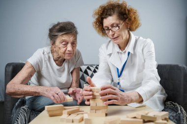 Jenga oynayan yaşlı kadın, bloklardan kule inşa ediyor. Beyaz laboratuvar önlüklü yaşlı doktor, kıdemli hastayı destekliyor, mantık geliştiriyor, iyi motor beceriler geliştiriyor, evde yaşlı yalnız kadın hastalıkları var..