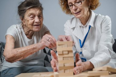 Bunama terapisi, parmaklar ve motor beceriler geliştirmek, kuleye tahta bloklar yapmak, Jenga oynamak. Yaşlı kadın 90 yaşında ve doktor huzurevinde eğitim oyunu oynuyor.