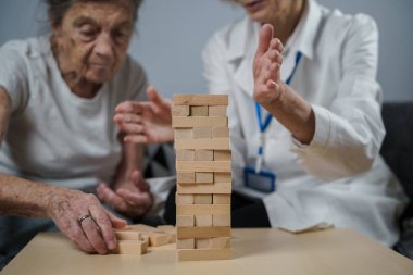 Bunama terapisi, parmaklar ve motor beceriler geliştirmek, kuleye tahta bloklar yapmak, Jenga oynamak. Yaşlı kadın 90 yaşında ve doktor huzurevinde eğitim oyunu oynuyor.