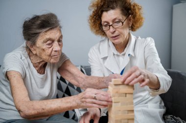 Bunama terapisi, parmaklar ve motor beceriler geliştirmek, kuleye tahta bloklar yapmak, Jenga oynamak. Yaşlı kadın 90 yaşında ve doktor huzurevinde eğitim oyunu oynuyor.