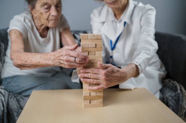 Bunama terapisi, parmaklar ve motor beceriler geliştirmek, kuleye tahta bloklar yapmak, Jenga oynamak. Yaşlı kadın 90 yaşında ve doktor huzurevinde eğitim oyunu oynuyor.