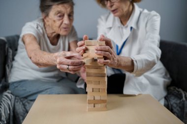 Bunama terapisi, parmaklar ve motor beceriler geliştirmek, kuleye tahta bloklar yapmak, Jenga oynamak. Yaşlı kadın 90 yaşında ve doktor huzurevinde eğitim oyunu oynuyor.