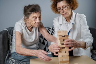 Bunama terapisi, parmaklar ve motor beceriler geliştirmek, kuleye tahta bloklar yapmak, Jenga oynamak. Yaşlı kadın 90 yaşında ve doktor huzurevinde eğitim oyunu oynuyor.