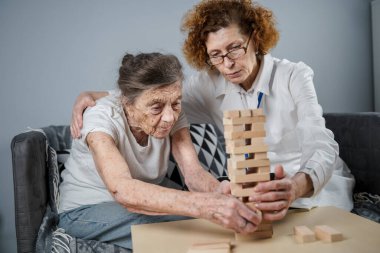 Bunama terapisi, parmaklar ve motor beceriler geliştirmek, kuleye tahta bloklar yapmak, Jenga oynamak. Yaşlı kadın 90 yaşında ve doktor huzurevinde eğitim oyunu oynuyor.