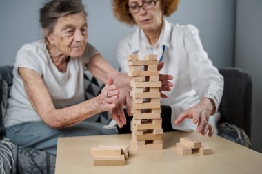 Bunama terapisi, parmaklar ve motor beceriler geliştirmek, kuleye tahta bloklar yapmak, Jenga oynamak. Yaşlı kadın 90 yaşında ve doktor huzurevinde eğitim oyunu oynuyor.