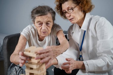 Jenga oynayan yaşlı kadın, bloklardan kule inşa ediyor. Beyaz laboratuvar önlüklü yaşlı doktor, kıdemli hastayı destekliyor, mantık geliştiriyor, iyi motor beceriler geliştiriyor, evde yaşlı yalnız kadın hastalıkları var..