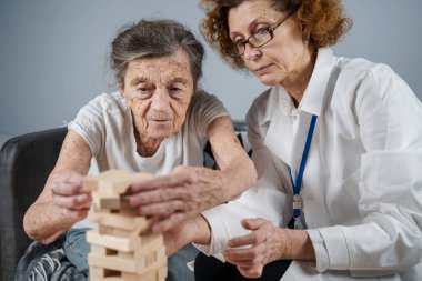 Bunama terapisi, parmaklar ve motor beceriler geliştirmek, kuleye tahta bloklar yapmak, Jenga oynamak. Yaşlı kadın 90 yaşında ve doktor huzurevinde eğitim oyunu oynuyor.
