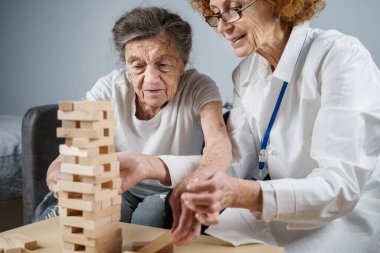Bunama terapisi, parmaklar ve motor beceriler geliştirmek, kuleye tahta bloklar yapmak, Jenga oynamak. Yaşlı kadın 90 yaşında ve doktor huzurevinde eğitim oyunu oynuyor.