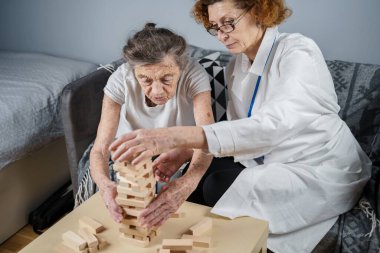 Bunama terapisi, parmaklar ve motor beceriler geliştirmek, kuleye tahta bloklar yapmak, Jenga oynamak. Yaşlı kadın 90 yaşında ve doktor huzurevinde eğitim oyunu oynuyor.
