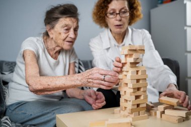 Jenga oynayan yaşlı kadın, bloklardan kule inşa ediyor. Beyaz laboratuvar önlüklü yaşlı doktor, kıdemli hastayı destekliyor, mantık geliştiriyor, iyi motor beceriler geliştiriyor, evde yaşlı yalnız kadın hastalıkları var..
