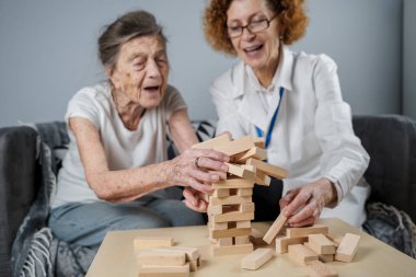 Jenga oynayan yaşlı kadın, bloklardan kule inşa ediyor. Beyaz laboratuvar önlüklü yaşlı doktor, kıdemli hastayı destekliyor, mantık geliştiriyor, iyi motor beceriler geliştiriyor, evde yaşlı yalnız kadın hastalıkları var..
