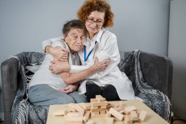 Jenga oynayan yaşlı kadın, bloklardan kule inşa ediyor. Beyaz laboratuvar önlüklü yaşlı doktor, kıdemli hastayı destekliyor, mantık geliştiriyor, iyi motor beceriler geliştiriyor, evde yaşlı yalnız kadın hastalıkları var..