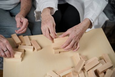 Jenga oyunu. Temaları bunama, yaşlanma ve yaşlılar için oyunlar. Kafkasyalı son sınıf öğrencisi kadın, bir hastanın evindeki terapi ve jenga oyununun bir parçası olarak bir doktorun yardımıyla ahşap bloklardan kule inşa ediyor..