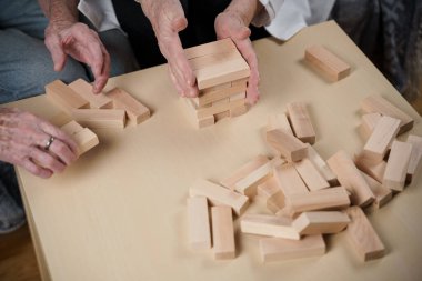 Jenga oyunu. Temaları bunama, yaşlanma ve yaşlılar için oyunlar. Kafkasyalı son sınıf öğrencisi kadın, bir hastanın evindeki terapi ve jenga oyununun bir parçası olarak bir doktorun yardımıyla ahşap bloklardan kule inşa ediyor..
