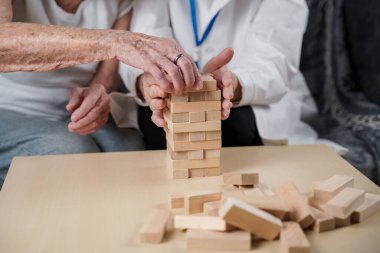 Jenga oynayan yaşlı kadın, bloklardan kule inşa ediyor. Beyaz laboratuvar önlüklü yaşlı doktor, kıdemli hastayı destekliyor, mantık geliştiriyor, iyi motor beceriler geliştiriyor, evde yaşlı yalnız kadın hastalıkları var..
