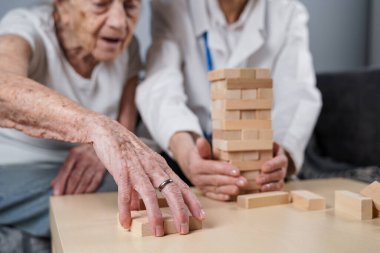 Jenga oynayan yaşlı kadın, bloklardan kule inşa ediyor. Beyaz laboratuvar önlüklü yaşlı doktor, kıdemli hastayı destekliyor, mantık geliştiriyor, iyi motor beceriler geliştiriyor, evde yaşlı yalnız kadın hastalıkları var..