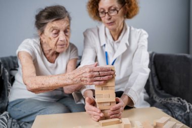 Jenga oynayan yaşlı kadın, bloklardan kule inşa ediyor. Beyaz laboratuvar önlüklü yaşlı doktor, kıdemli hastayı destekliyor, mantık geliştiriyor, iyi motor beceriler geliştiriyor, evde yaşlı yalnız kadın hastalıkları var..