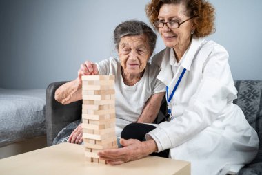 Bunama terapisi, parmaklar ve motor beceriler geliştirmek, kuleye tahta bloklar yapmak, Jenga oynamak. Yaşlı kadın 90 yaşında ve doktor huzurevinde eğitim oyunu oynuyor.