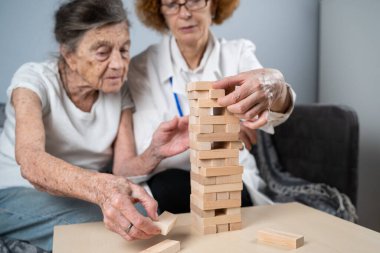 Jenga oynayan yaşlı kadın, bloklardan kule inşa ediyor. Beyaz laboratuvar önlüklü yaşlı doktor, kıdemli hastayı destekliyor, mantık geliştiriyor, iyi motor beceriler geliştiriyor, evde yaşlı yalnız kadın hastalıkları var..