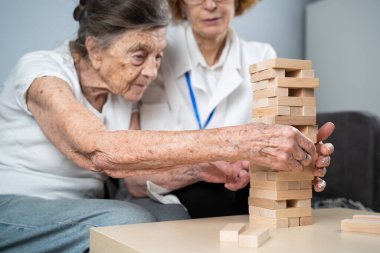 Bunama terapisi, parmaklar ve motor beceriler geliştirmek, kuleye tahta bloklar yapmak, Jenga oynamak. Yaşlı kadın 90 yaşında ve doktor huzurevinde eğitim oyunu oynuyor.
