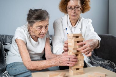 Bunama terapisi, parmaklar ve motor beceriler geliştirmek, kuleye tahta bloklar yapmak, Jenga oynamak. Yaşlı kadın 90 yaşında ve doktor huzurevinde eğitim oyunu oynuyor.