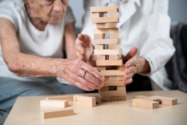 Bunama terapisi, parmaklar ve motor beceriler geliştirmek, kuleye tahta bloklar yapmak, Jenga oynamak. Yaşlı kadın 90 yaşında ve doktor huzurevinde eğitim oyunu oynuyor.