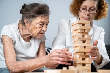 Jenga oynayan yaşlı kadın, bloklardan kule inşa ediyor. Beyaz laboratuvar önlüklü yaşlı doktor, kıdemli hastayı destekliyor, mantık geliştiriyor, iyi motor beceriler geliştiriyor, evde yaşlı yalnız kadın hastalıkları var..