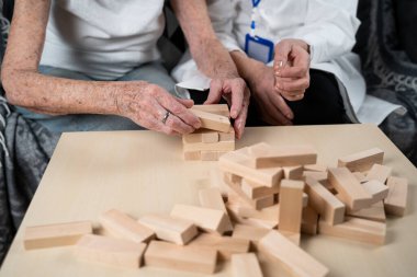 Jenga oynayan yaşlı kadın, bloklardan kule inşa ediyor. Beyaz laboratuvar önlüklü yaşlı doktor, kıdemli hastayı destekliyor, mantık geliştiriyor, iyi motor beceriler geliştiriyor, evde yaşlı yalnız kadın hastalıkları var..