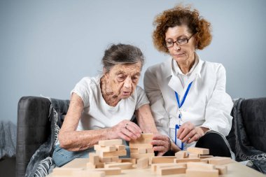 Jenga oynayan yaşlı kadın, bloklardan kule inşa ediyor. Beyaz laboratuvar önlüklü yaşlı doktor, kıdemli hastayı destekliyor, mantık geliştiriyor, iyi motor beceriler geliştiriyor, evde yaşlı yalnız kadın hastalıkları var..