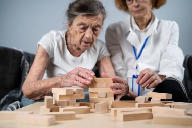 Bunama terapisi, parmaklar ve motor beceriler geliştirmek, kuleye tahta bloklar yapmak, Jenga oynamak. Yaşlı kadın 90 yaşında ve doktor huzurevinde eğitim oyunu oynuyor.