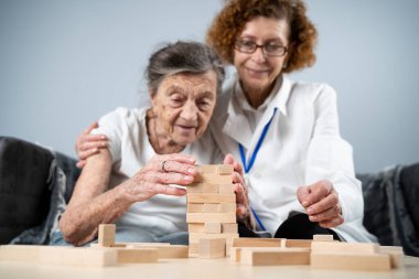 Jenga oynayan yaşlı kadın, bloklardan kule inşa ediyor. Beyaz laboratuvar önlüklü yaşlı doktor, kıdemli hastayı destekliyor, mantık geliştiriyor, iyi motor beceriler geliştiriyor, evde yaşlı yalnız kadın hastalıkları var..
