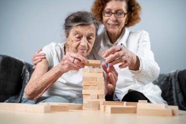 Bunama terapisi, parmaklar ve motor beceriler geliştirmek, kuleye tahta bloklar yapmak, Jenga oynamak. Yaşlı kadın 90 yaşında ve doktor huzurevinde eğitim oyunu oynuyor.