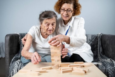 Jenga oynayan yaşlı kadın, bloklardan kule inşa ediyor. Beyaz laboratuvar önlüklü yaşlı doktor, kıdemli hastayı destekliyor, mantık geliştiriyor, iyi motor beceriler geliştiriyor, evde yaşlı yalnız kadın hastalıkları var..