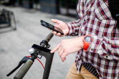 Akıllı telefon tutan eller, yakın plan elektrikli scooter kiralama kilidini açar. Şehirde çevre dostu alternatif ulaşım, trafikte kişisel hareketlilik. Şehir sakinleri tarafından geliştirilmiş aygıtlar.