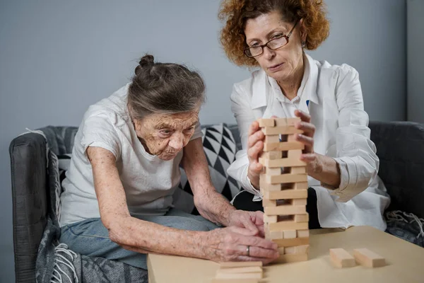 Jenga oynayan yaşlı kadın, bloklardan kule inşa ediyor. Beyaz laboratuvar önlüklü yaşlı doktor, kıdemli hastayı destekliyor, mantık geliştiriyor, iyi motor beceriler geliştiriyor, evde yaşlı yalnız kadın hastalıkları var..