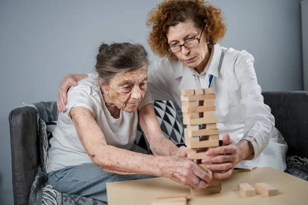 Bunama terapisi, parmaklar ve motor beceriler geliştirmek, kuleye tahta bloklar yapmak, Jenga oynamak. Yaşlı kadın 90 yaşında ve doktor huzurevinde eğitim oyunu oynuyor.