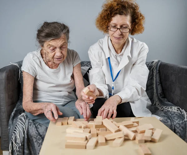 Jenga oynayan yaşlı kadın, bloklardan kule inşa ediyor. Beyaz laboratuvar önlüklü yaşlı doktor, kıdemli hastayı destekliyor, mantık geliştiriyor, iyi motor beceriler geliştiriyor, evde yaşlı yalnız kadın hastalıkları var..