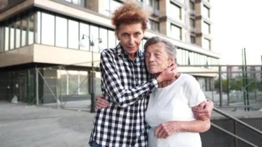 Bağlılık. Şehirde dolaşmak için mükemmel bir arkadaş. Bakıcı, gönüllü asistan yaşlı bayanla ilgileniyor. Kızı olan yaşlı bir kadın çok katlı binanın avlusunda el ele tutuşup sarılıyor.