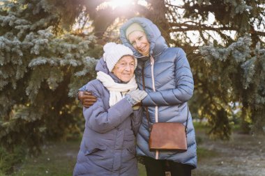 Mutlu aile kavramı, yaşlılık, duygular, emeklilik yaşında yaşlı bakım. Aktif kıdemli büyükanne ve yetişkin kız kışın ormanda Noel ağacının arka planına sarılıyorlar..