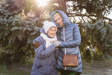 Kafkasyalı olgun kadın ve yaşlı kadın, Noel ve yeni yıl tatillerinde birlikte vakit geçirmekten mutlu olurlar. Güneşli havalarda, köknar ağacının arka planında gülümseyerek ve kucaklaşarak..