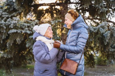 Mutlu aile kavramı, yaşlılık, duygular, emeklilik yaşında yaşlı bakım. Aktif kıdemli büyükanne ve yetişkin kız kışın ormanda Noel ağacının arka planına sarılıyorlar..