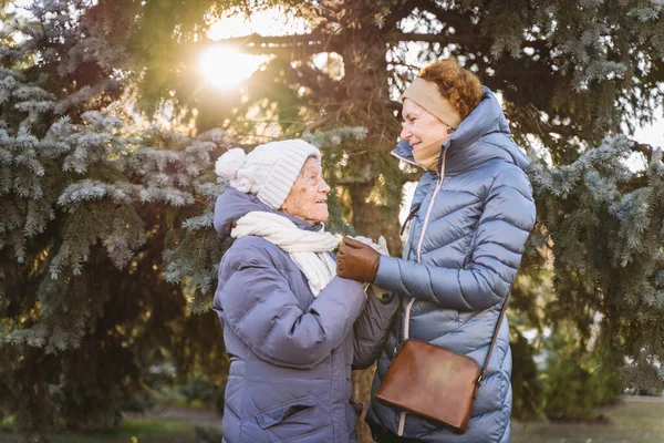 Motherhood. Theme importance visiting and spending time with old single parents during holidays. Senior mom and mature daughter happy family hug and laugh in park background Christmas tree in winter.