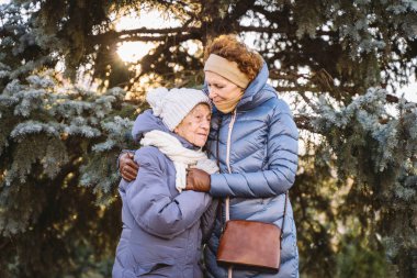 Annelik. Temanın önemi, bayramlarda yaşlı bekar ebeveynleri ziyaret etmek ve onlarla vakit geçirmek. Büyük anne ve yetişkin kız mutlu aile kucaklaşması ve gülüşmeler Park arka planında kışın Noel ağacı.